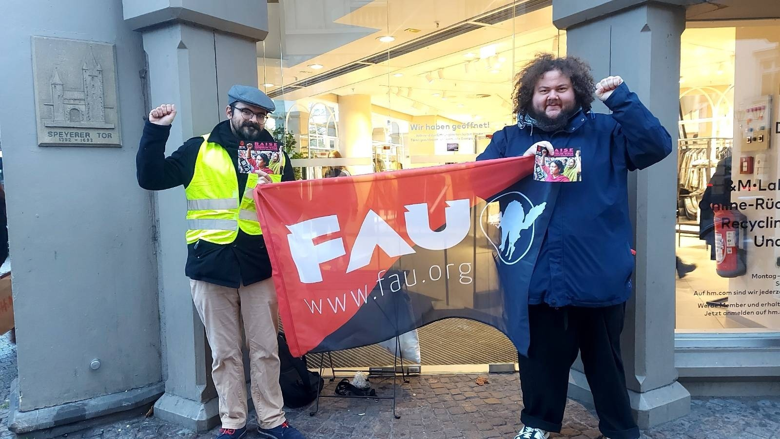 Zwei Personen die ein Banner der FAU halten. Beide Personen haben Flyer in der Hand.